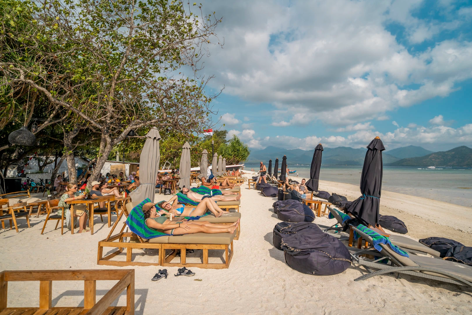 Loungers and low tables on the sand at a beach club on Gili Air, with Lombok across the water